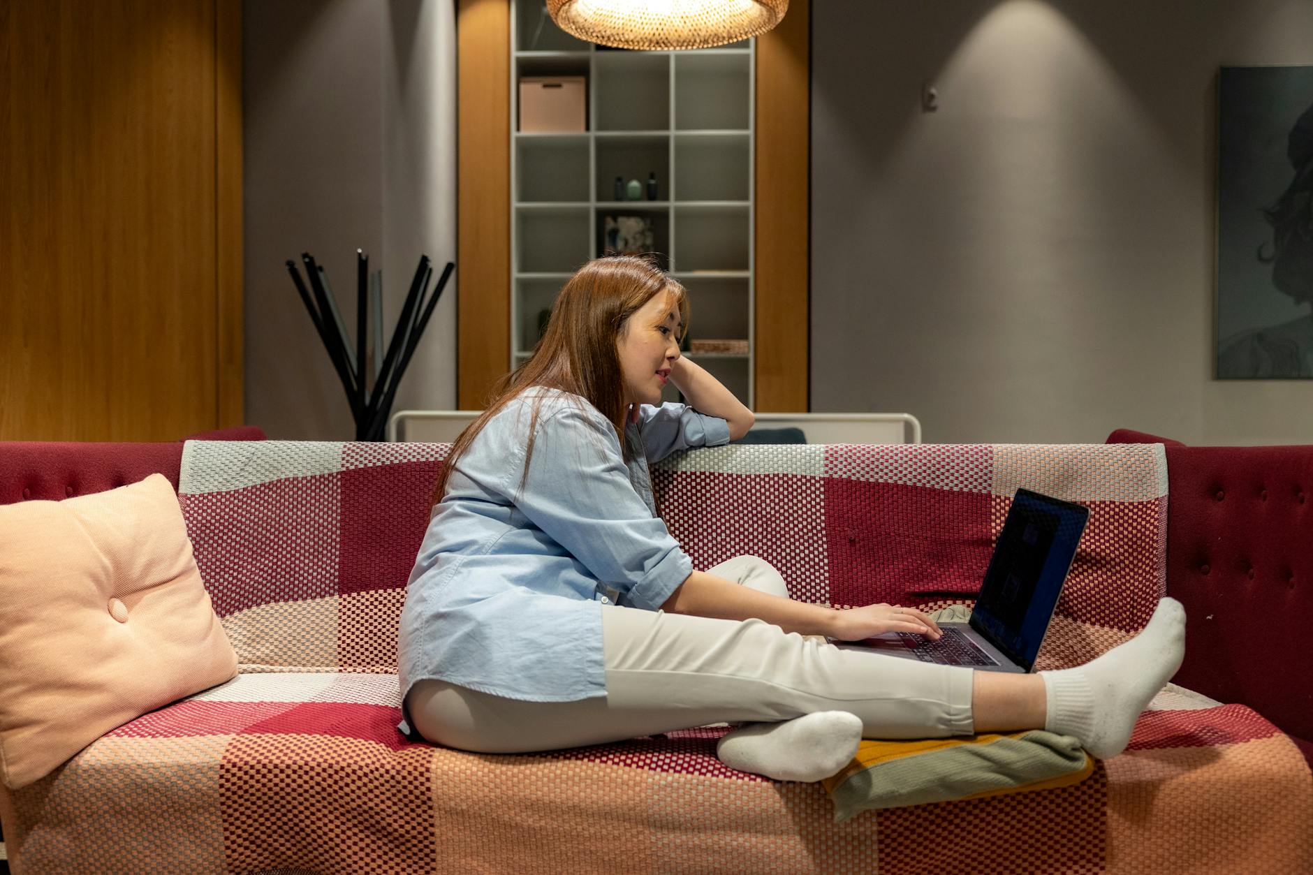 young woman sits up to do laptop work in relaxing environment while working from home