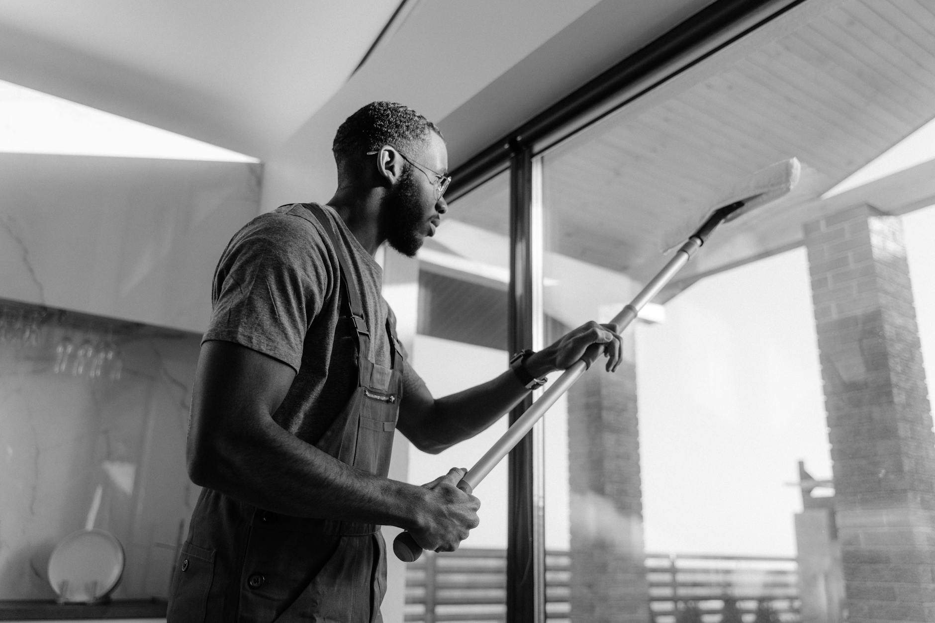 grayscale photo of a man cleaning a glass panel