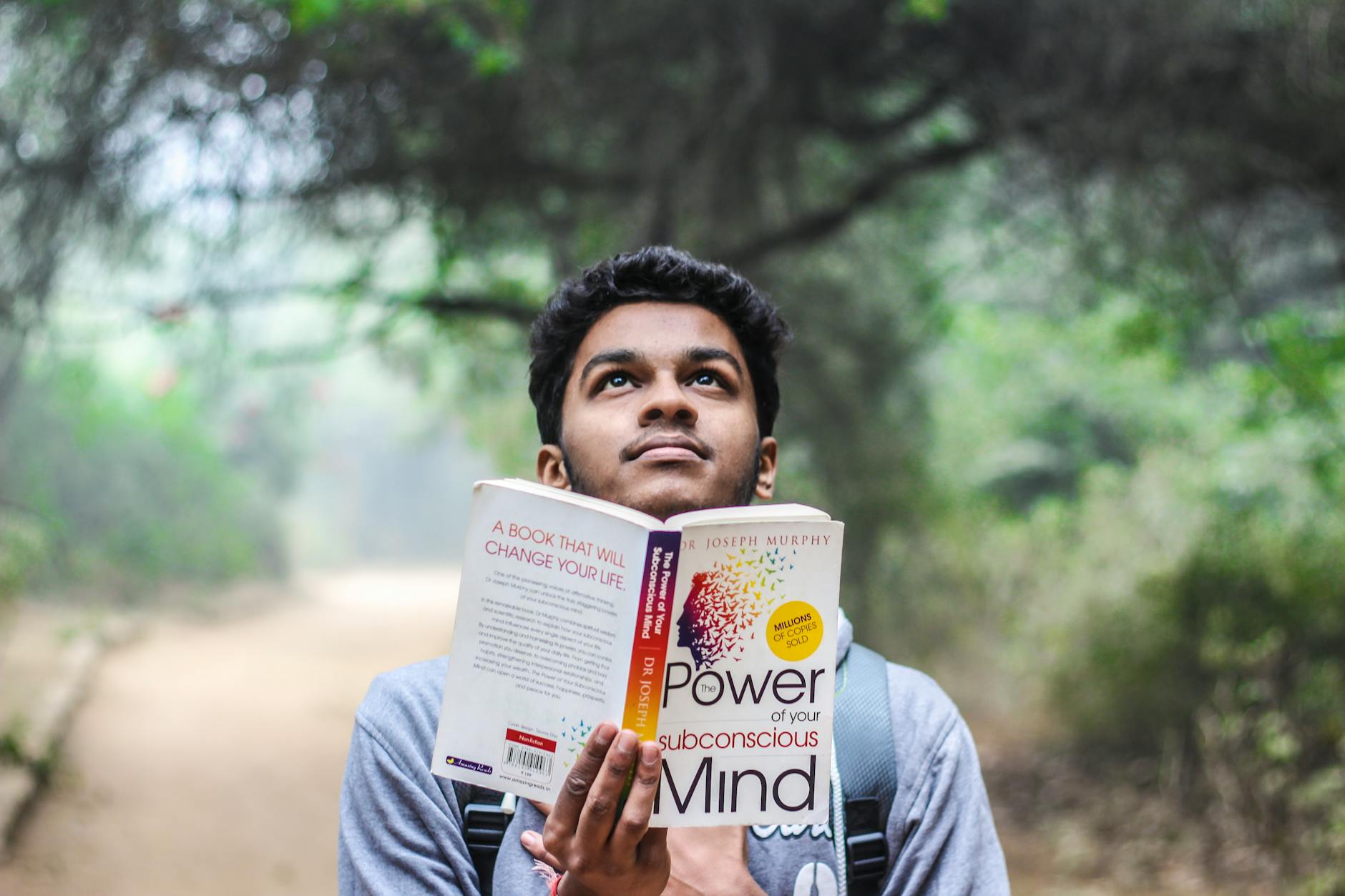 man in grey shirt holding opened book looking upward